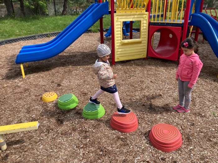 Two kids wearing hats and jackets are having fun on the playground in EarlyON Years Centre