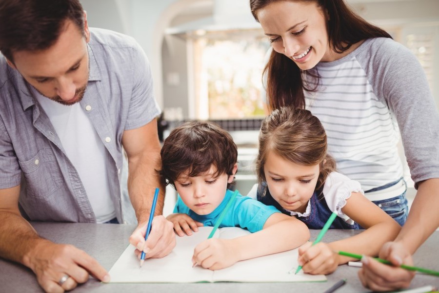 Parents with their daughter and son are writing in the copybook together